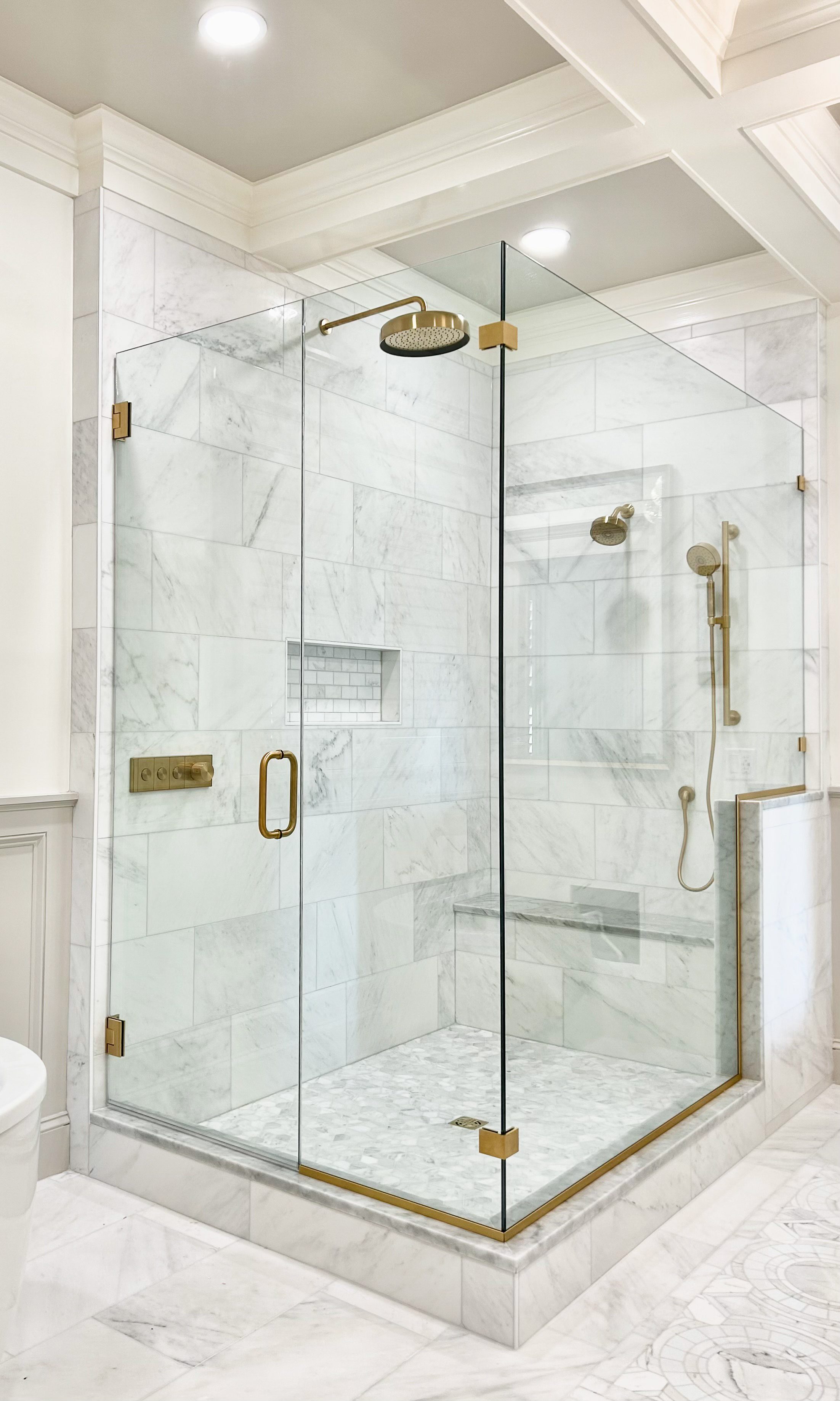 Frameless glass corner shower enclosure in Carrara marble with brass hardware