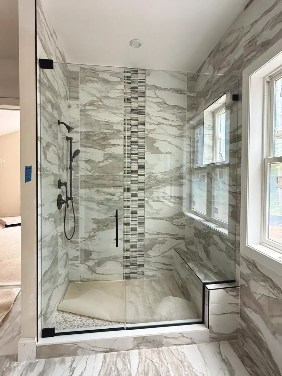Door and panel frameless glass shower enclosure, matte black hardware, black sweep