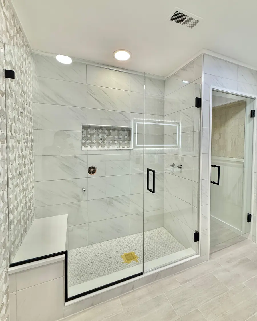 Door and panel frameless glass shower enclosure, matte black hardware, with a water closet door