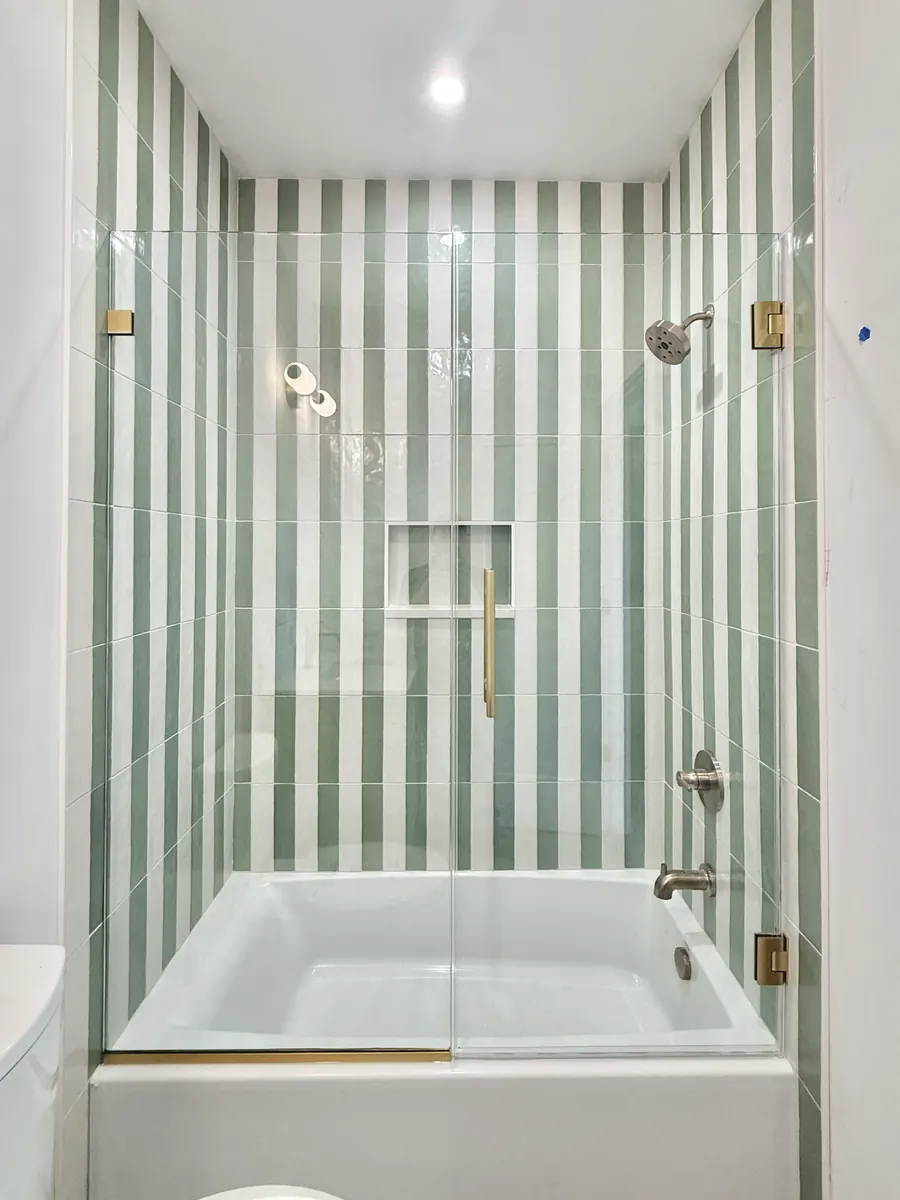Door and panel frameless glass shower enclosure, over a tub, satin brass hardware