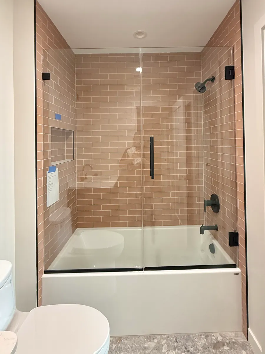 Door and panel frameless glass shower enclosure, over a tub, matte black hardware