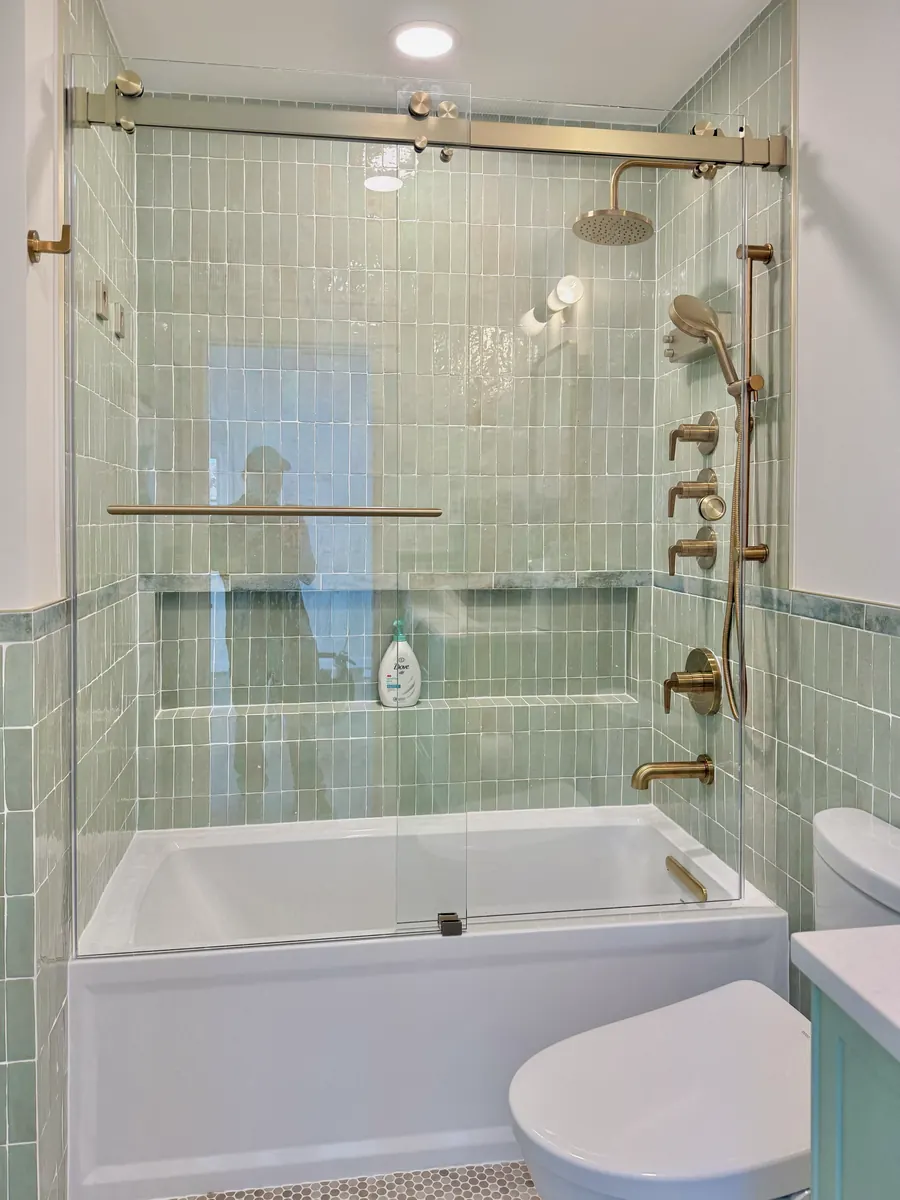Titan Duo series frameless sliding shower door, over a tub, brushed bronze hardware